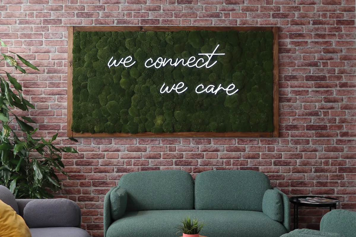 Moosbild mit leuchtendem Schriftzug vor einer Backsteinwand.